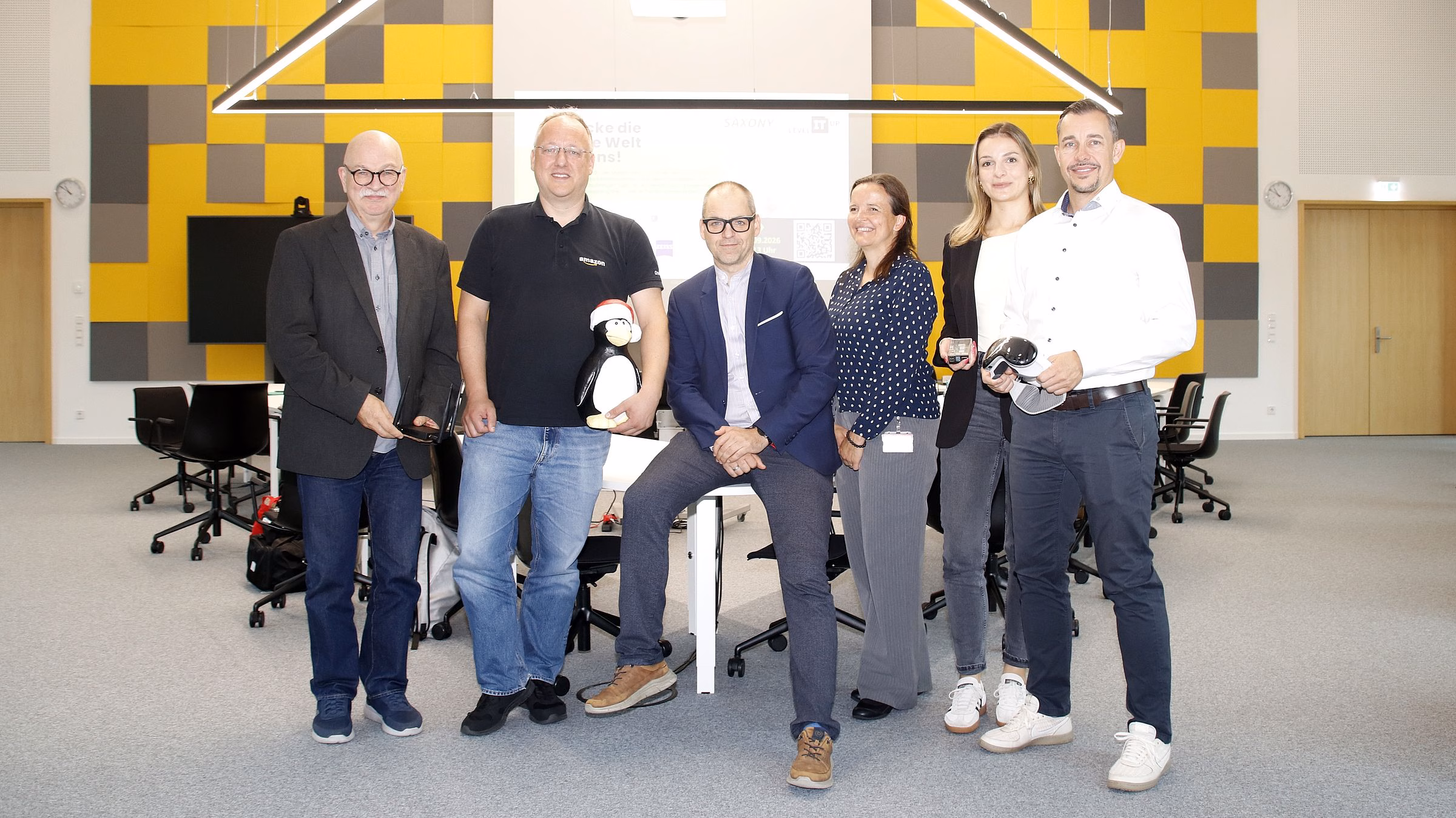 Schnuppertag zum „Level IT up“-Tag 2026. Es laden ein (von links nach rechts): Friedemann Höller (Eigenbetrieb IT Landeshauptstadt Dresden), Andreas Stieger (AWS Development Center Germany – hier mit Linux-Pinguin), Frank Bösenberg (Silicon Saxony – hier mit Augmented-Reality-Brille), Jenny Wätzig (SachsenEnergie), Anne-Sophie Graf (Communardo) und René Wohllebe (SAP). Foto: J. Frintert